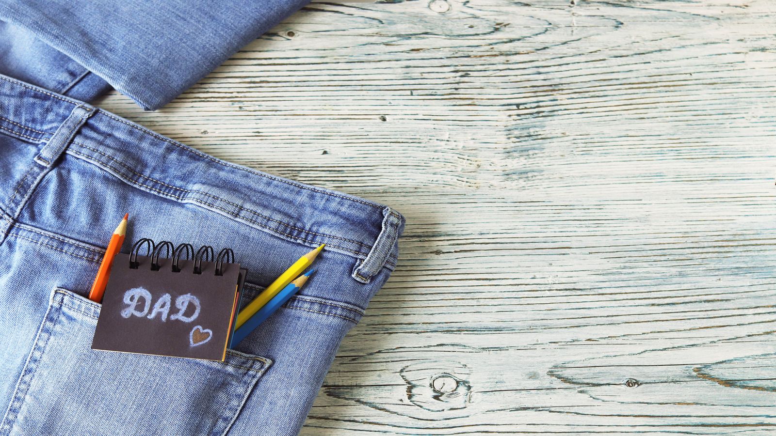 Neatly folded stack of repaired denim and cotton garments on a wooden work surface